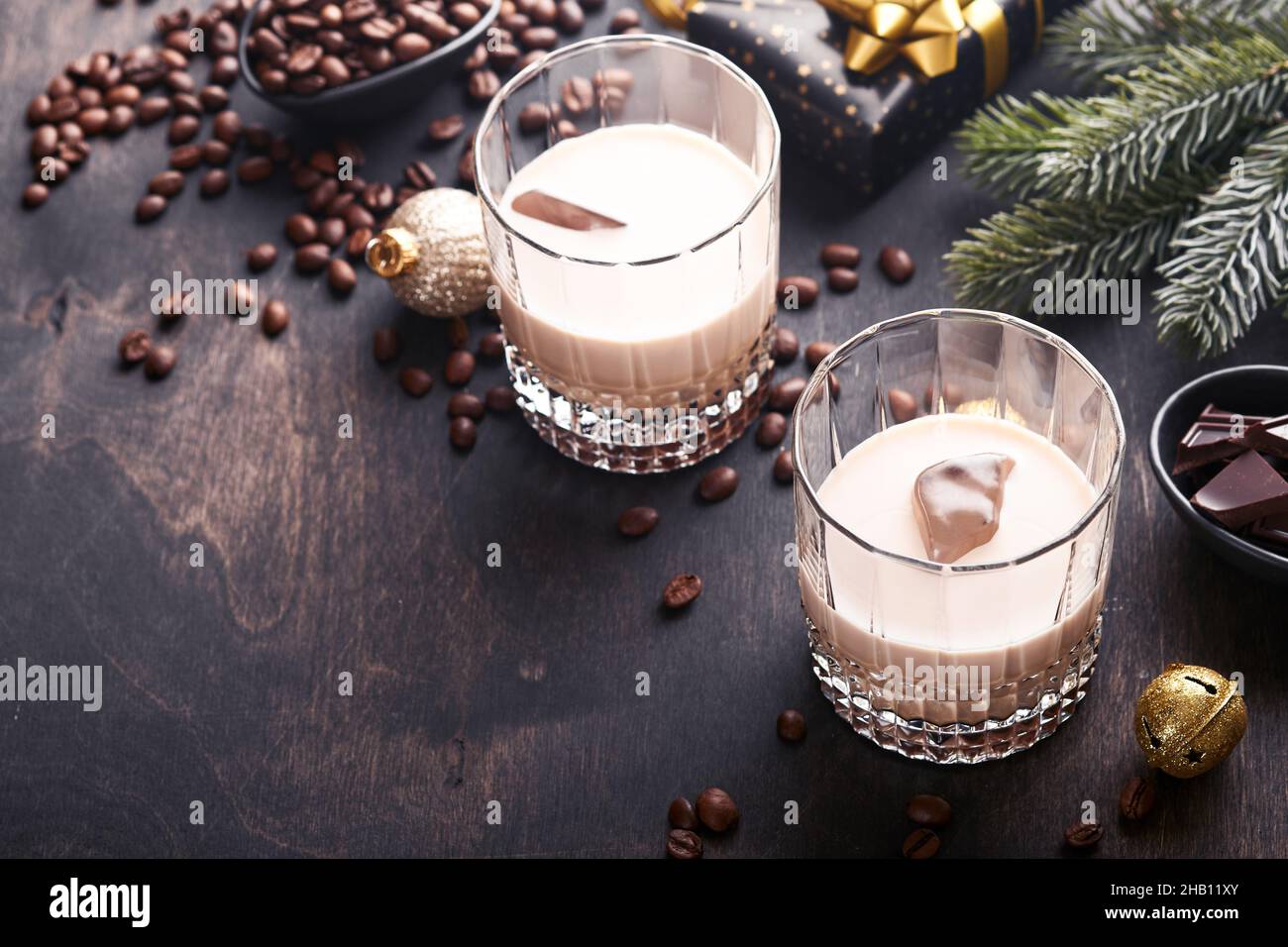 Bicchiere di crema irlandese liquore baileys con ghiaccio, caffè torrefatto in chicchi, cannella, decorazioni natalizie e cioccolato su tavola di fondo in legno scuro. Chris Foto Stock