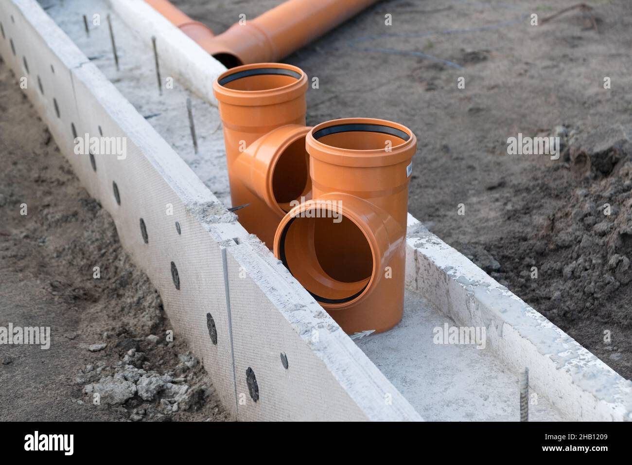 Angolo del tubo fognario sul cantiere. Nuovo tubo di drenaggio in plastica PVC arancione Foto Stock