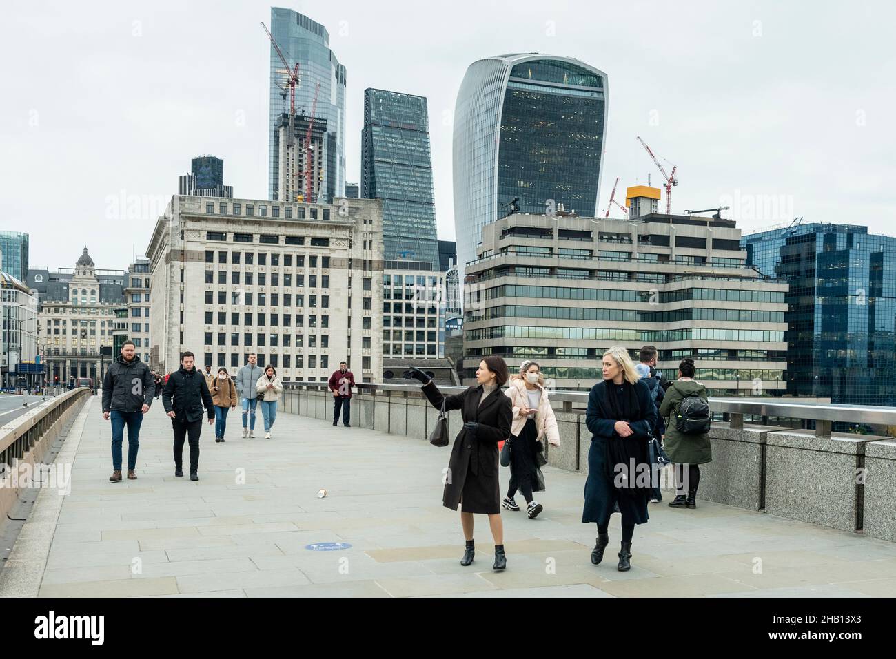 Londra, Regno Unito. 16 dicembre 2021. La gente attraversa il London Bridge con i grattacieli della City of London in lontananza. La Banca d'Inghilterra ha annunciato che ha aumentato il tasso d'interesse dal 0,1% al 0,25% in risposta all'aumento dell'inflazione al 5,1% e hanno già previsto che il tasso d'inflazione salirà al 6% il prossimo anno. Credit: Stephen Chung / Alamy Live News Foto Stock