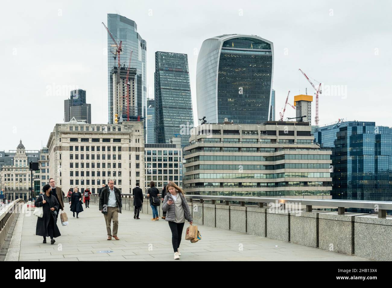 Londra, Regno Unito. 16 dicembre 2021. La gente attraversa il London Bridge con i grattacieli della City of London in lontananza. La Banca d'Inghilterra ha annunciato che ha aumentato il tasso d'interesse dal 0,1% al 0,25% in risposta all'aumento dell'inflazione al 5,1% e hanno già previsto che il tasso d'inflazione salirà al 6% il prossimo anno. Credit: Stephen Chung / Alamy Live News Foto Stock