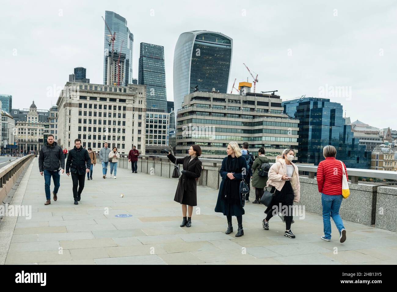 Londra, Regno Unito. 16 dicembre 2021. La gente attraversa il London Bridge con i grattacieli della City of London in lontananza. La Banca d'Inghilterra ha annunciato che ha aumentato il tasso d'interesse dal 0,1% al 0,25% in risposta all'aumento dell'inflazione al 5,1% e hanno già previsto che il tasso d'inflazione salirà al 6% il prossimo anno. Credit: Stephen Chung / Alamy Live News Foto Stock
