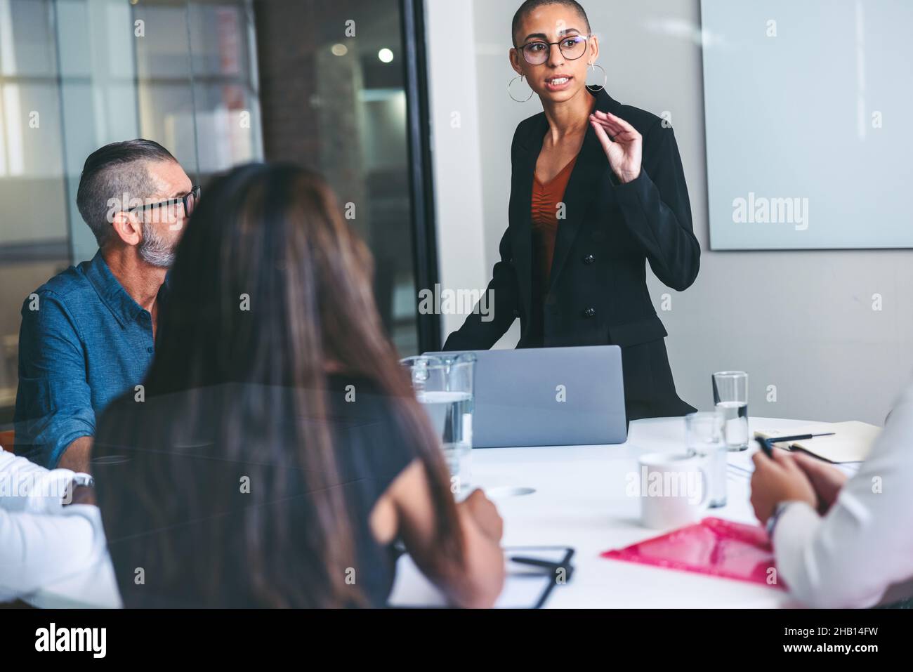 Giovane donna d'affari fiduciosa che presenta ai suoi colleghi in ufficio. Gruppo di uomini d'affari creativi che hanno un incontro in un lavoro moderno Foto Stock