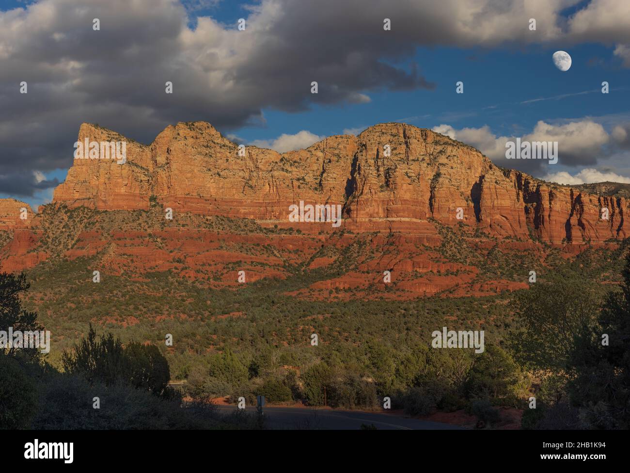 Ripido muro di roccia rossa di montagna e pineta contro le nuvole tempesta e la luna crescente panorama a Sedona, Arizona. Foto Stock