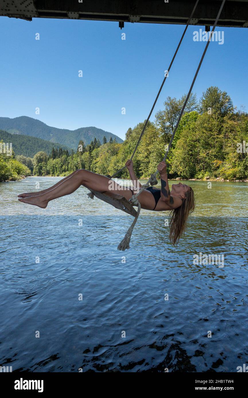 Fit femmina in bikini su un altalena su un fiume in montagna Foto Stock