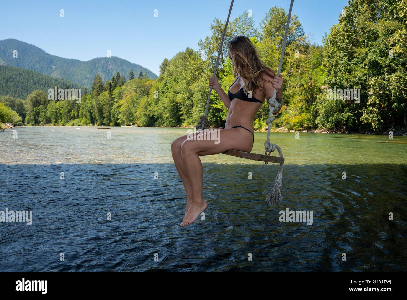 Fit donna in un bikini che oscilla su un fiume nelle montagne a cascata Foto Stock