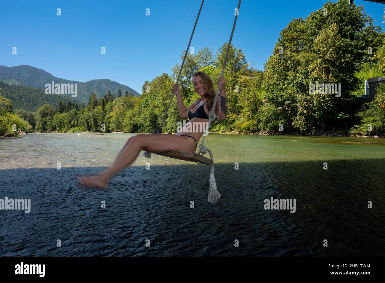 Donna che indossa un bikini su un'altalena sopra un fiume Foto Stock