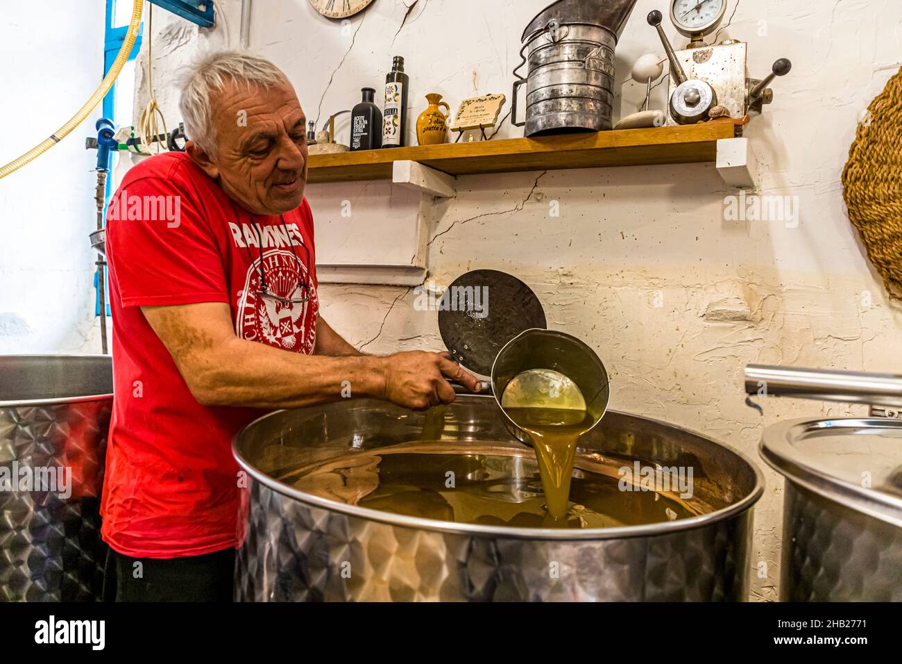 Il maestro di stampa Fabrice Godet versa olio d'oliva giallo-dorato da una cazzuola di metallo in un serbatoio in acciaio inossidabile presso il frantoio Moulin de Saint-Cassien a Draguignan, dipartimento di Var, Francia; dopo la spremitura, la miscela acqua-olio rimane scoperta per circa un'ora prima che lui raccolga l'olio galleggiante in superficie – l'acqua di frutta più pesante affonda sul fondo. Foto Stock