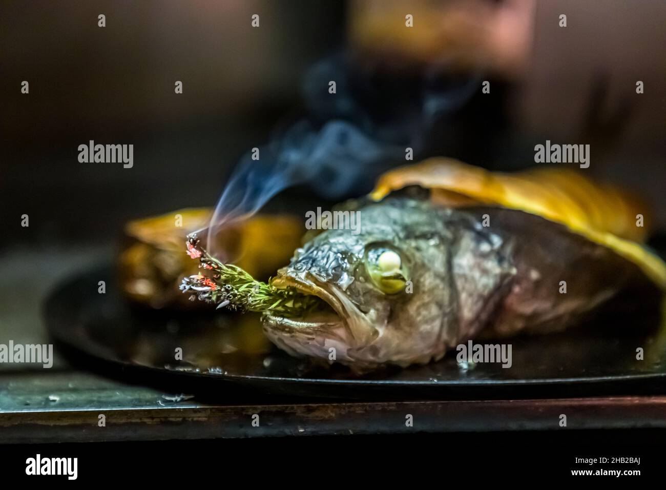 Il Loup de Mediterranée riempito con un souffle di Cyril Aveline delicatamente tartufato fuma ancora nella griglieria Josper con un rametto di rosmarino. Ristorante Hestia a Bormes-les-Mimosas, Francia Foto Stock