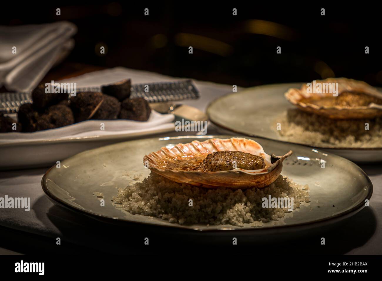 Capasanta in crosta di gheriglia e tartufo di Cyril Aveline, Ristorante Hestia a Bormes-les-Mimosas, Francia. Il piatto poggia su un letto di sale marino grossolano; un vassoio di tartufo nero è pronto, fuori fuoco, sullo sfondo. Foto Stock