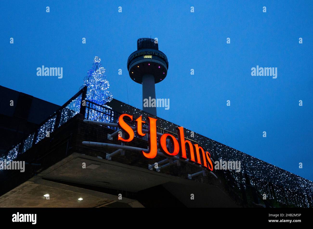 Insegna sull'ingresso del centro commerciale St Johns con la torre radio sopra e l'albero di luci di Natale Foto Stock