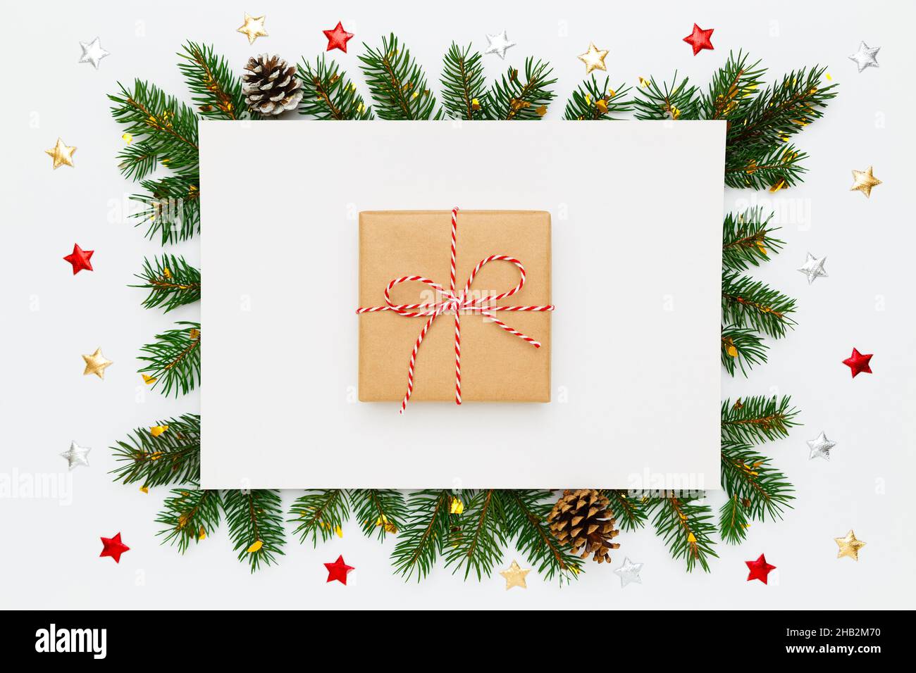Natale, Capodanno. Carta bianca bianca bianca bianca con regalo di Natale in carta artigianale al centro, in cornice di rami di abete naturale e pino Foto Stock