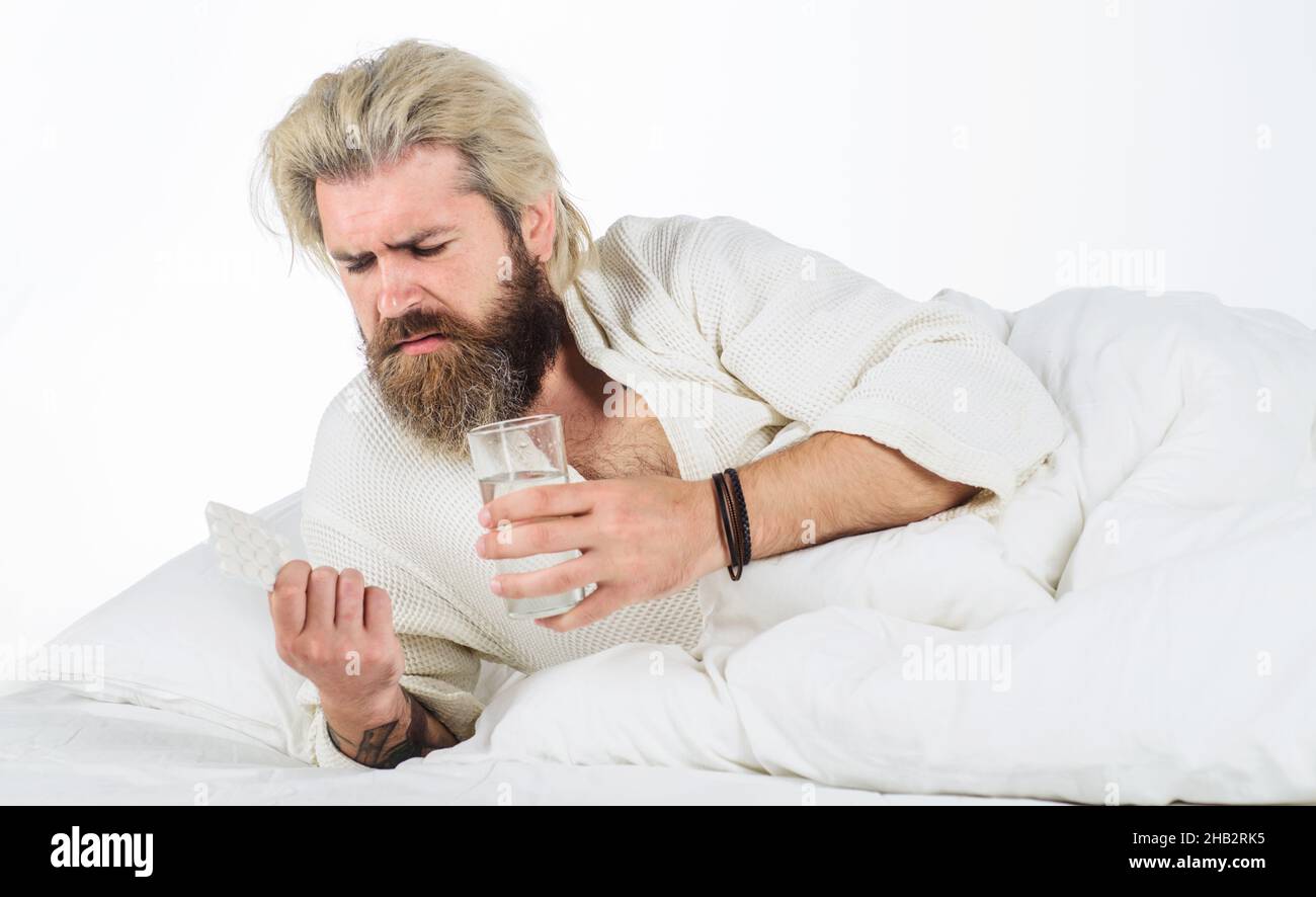 Uomo malato a letto con pillole bicchiere d'acqua. Influenza stagionale. Malattia. Maschio bearded che giace nel letto in casa. Foto Stock