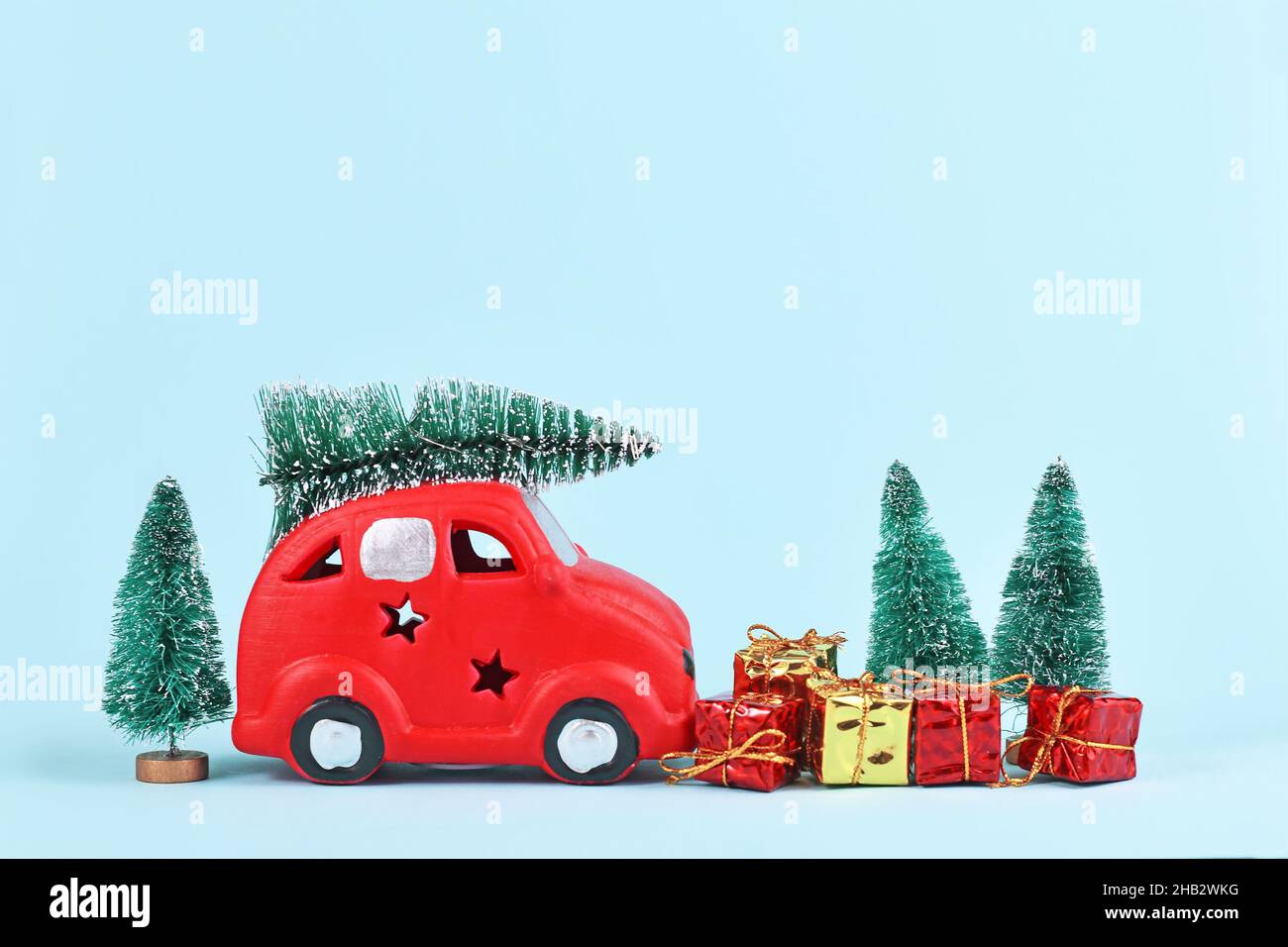 Auto rossa che trasporta le palle di neve dell'albero di natale e le scatole del regalo su sfondo blu con Foto Stock