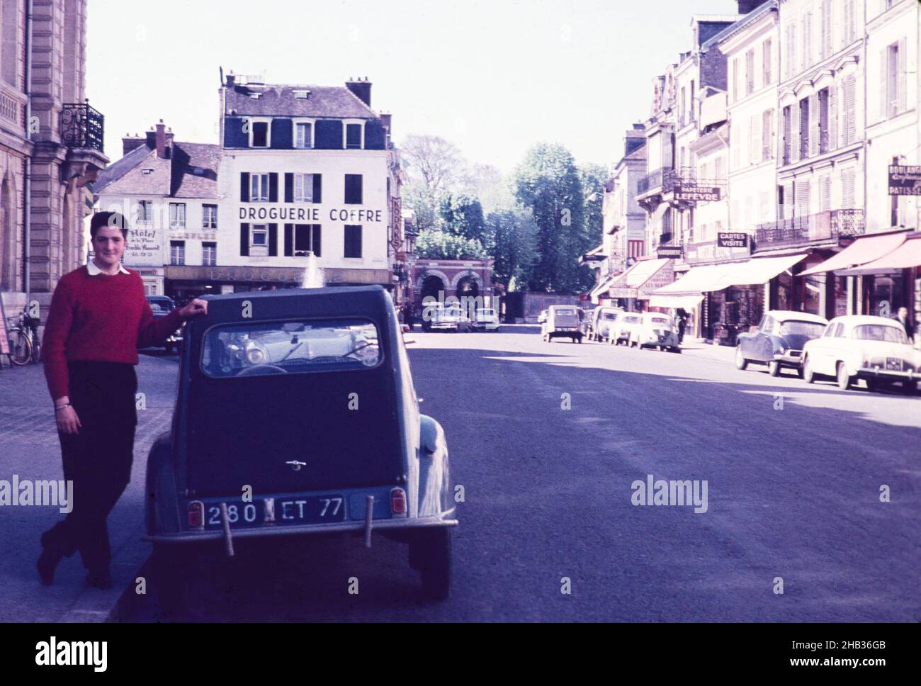 Giovane uomo in piedi contro Citroen 2CV auto in Rue Grande, Fontainebleau, Francia, c 1960 Foto Stock