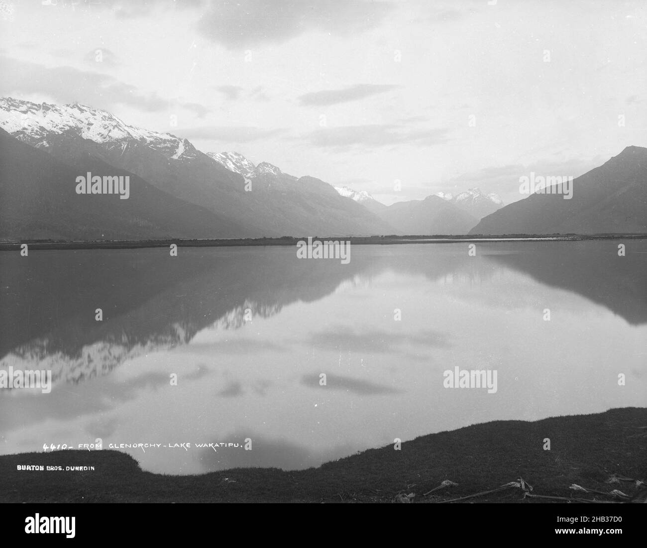 Da Glenorchy, Lake Wakatipu, studio Burton Brothers, studio fotografico, 1886, Dunedin, fotografia in bianco e nero, vista attraverso le acque calme e pianeggianti di un lago, con una catena montuosa innevata che corre sulla sinistra Foto Stock