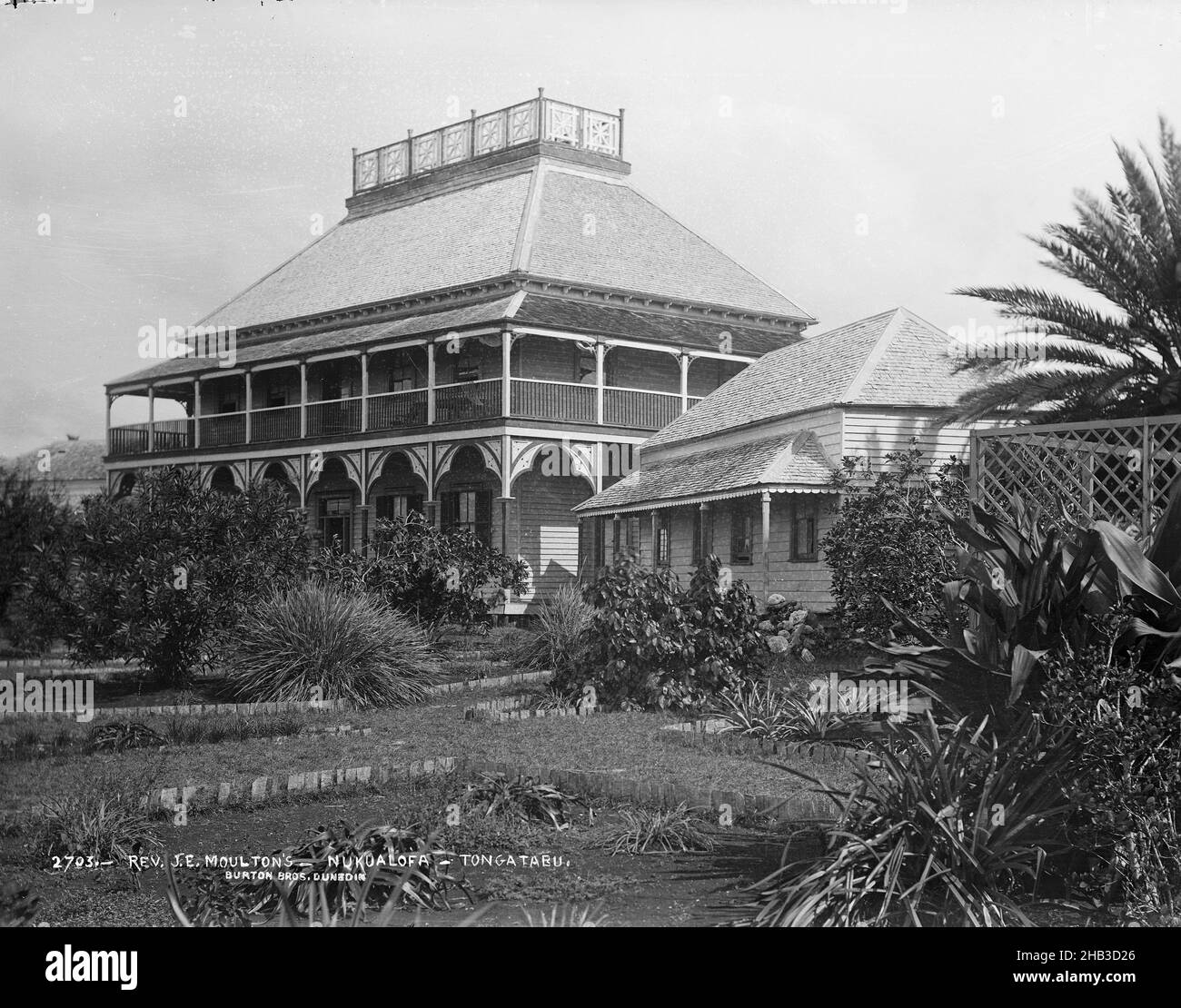 E. Moulton's, Nukualofa, Tongatabu [Nuku'alofa, Tongatapu], studio Burton Brothers, Studio fotografico, 29 luglio 1884, Nuova Zelanda, fotografia in bianco e nero, edifici coloniali, in primo piano vegetazione tropicale con giardino chiarificazione e traliccio recinzione. Edificio ad un piano con veranda a destra di un grandioso edificio a due piani con verande ad ogni piano. Un alto tetto a falde ha una piattaforma di osservazione con elaborate rotaie Foto Stock