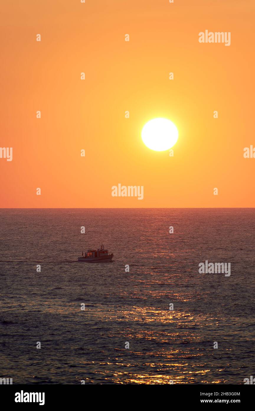 paesaggio di un tramonto arancione sull'orizzonte del mare, con le navi di ritorno al porto Foto Stock