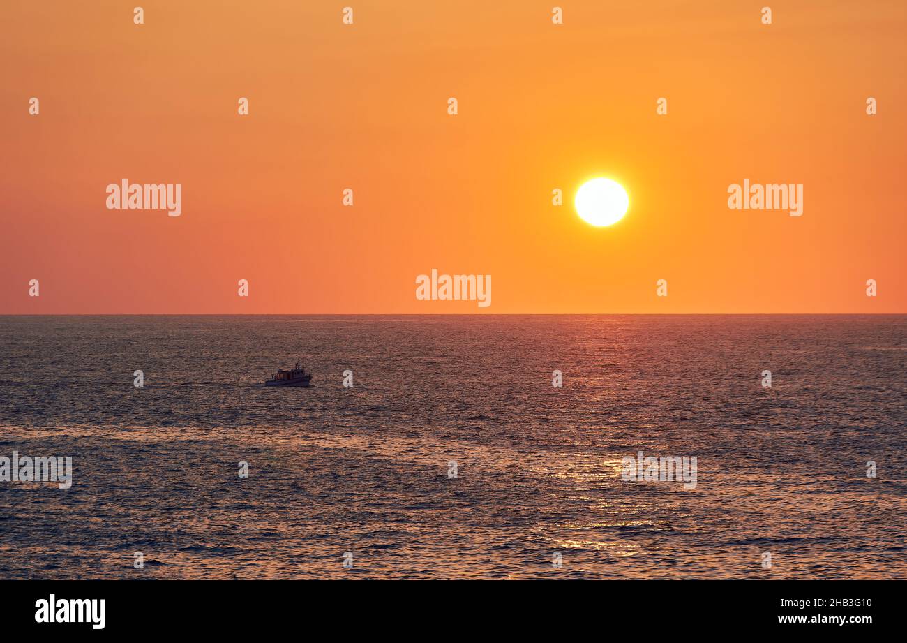 paesaggio di un tramonto arancione sull'orizzonte del mare, con le navi di ritorno al porto Foto Stock