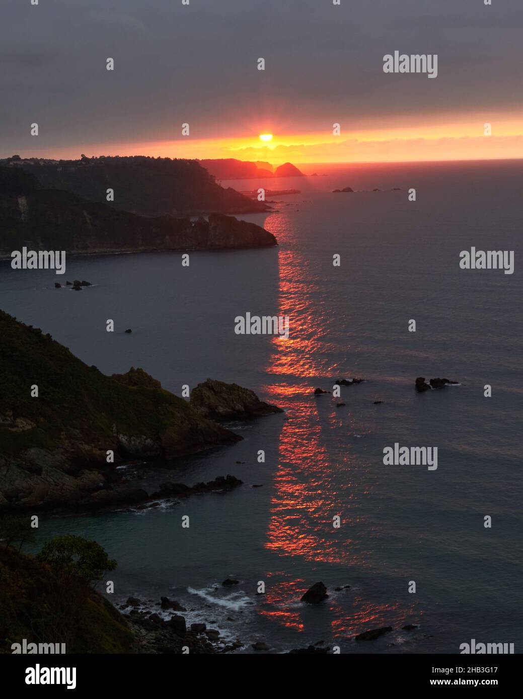paesaggio di un tramonto arancione sull'orizzonte del mare, i raggi passano attraverso la scogliera che si riflette nel mare Foto Stock