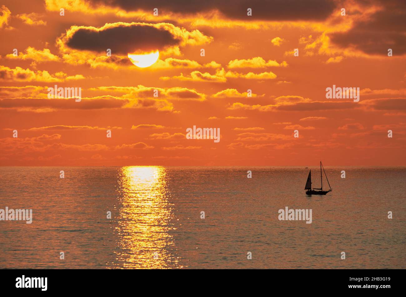 paesaggio di un tramonto arancione sull'orizzonte del mare, con le navi di ritorno al porto Foto Stock