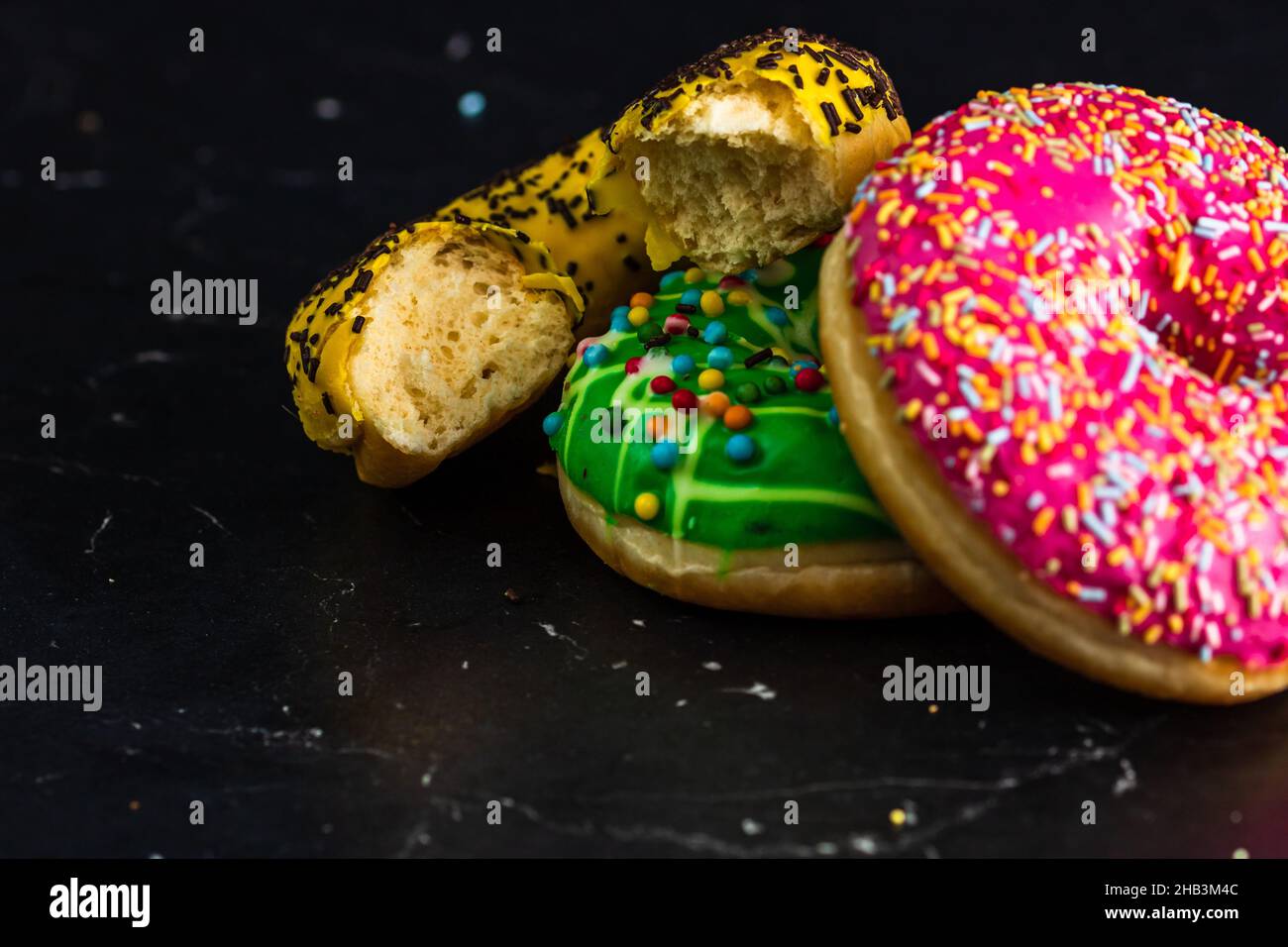 Primo piano di una ciambella bittata con due ciambelle colorate isolate su sfondo nero Foto Stock