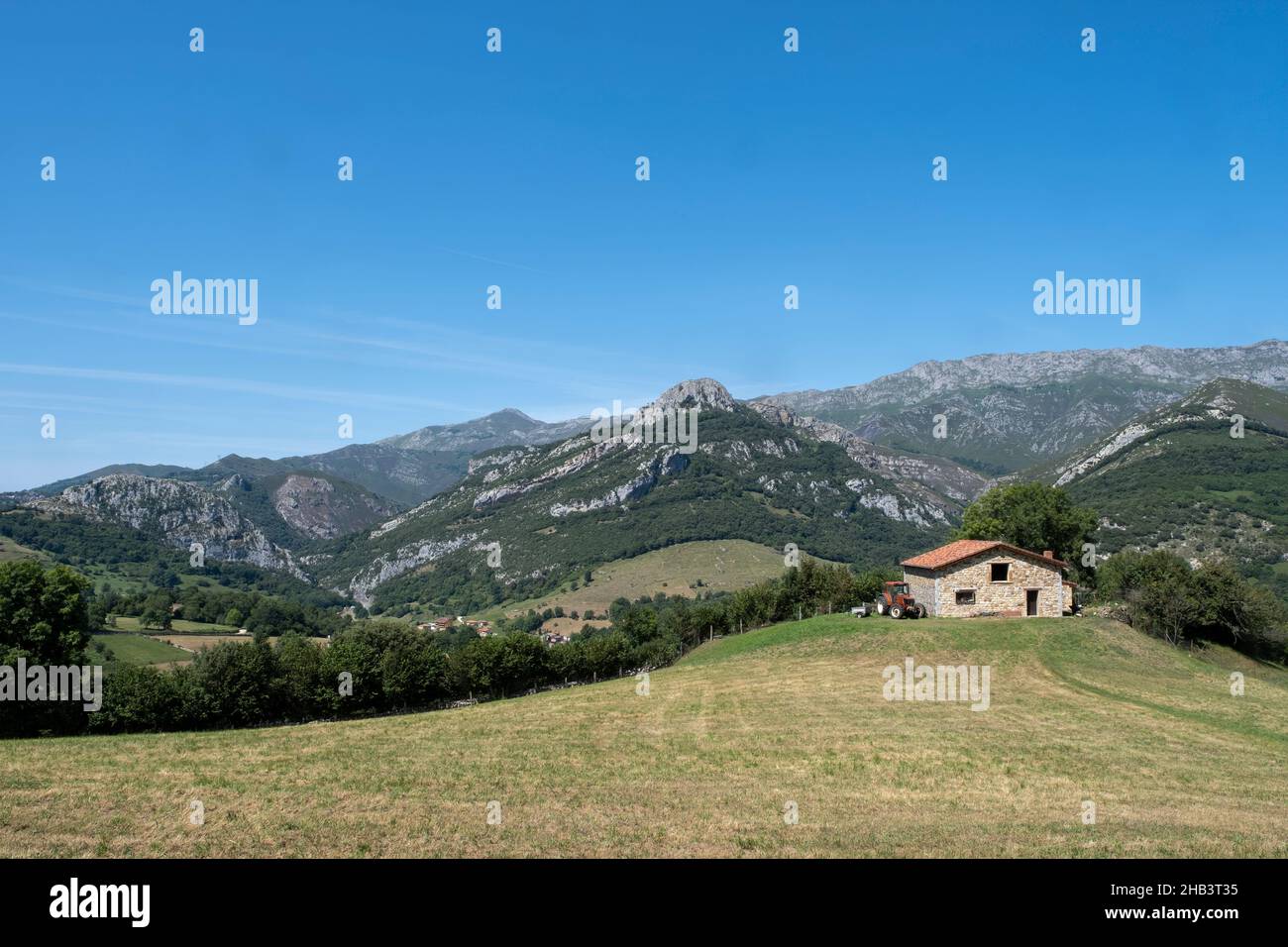 Campi in una zona montagnosa, con una casa colonica e un trattore con un rimorchio alla porta, Arenas de Cabrales, Asturias, Spagna, orizzontale Foto Stock