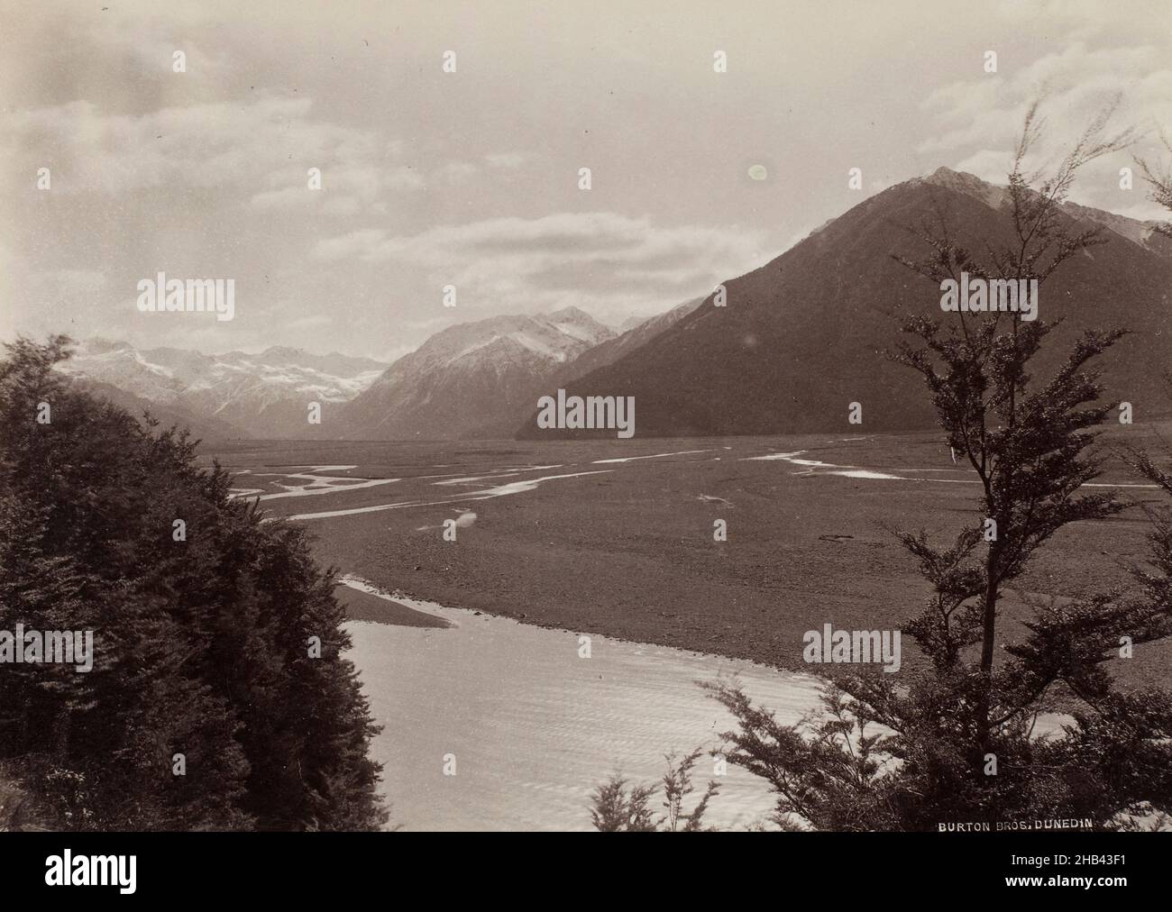 Bealey, West Coast Road, studio Burton Brothers, studio fotografico, Nuova Zelanda, Fotografia in bianco e nero, ampia vista da una collina della West Coast. Le catene montuose innevate riempiono lo sfondo dell'immagine, mentre una collina, ricoperta di cespugli e alberi, e un fiume, consumano la prua e la base centrale dell'immagine Foto Stock