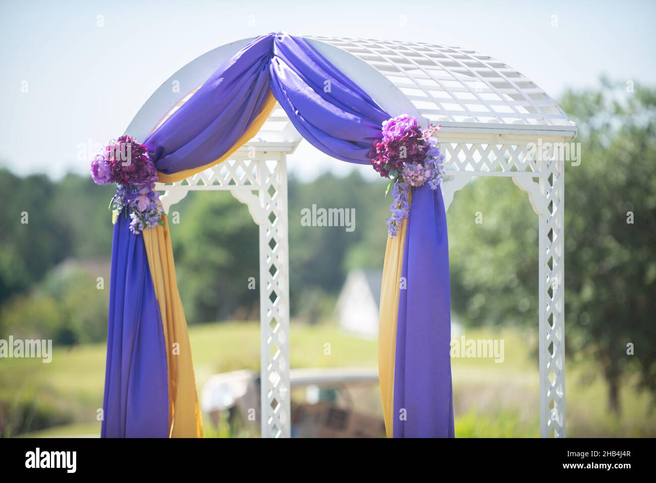 L'arco della cerimonia di nozze bianco magestico è stato fissato in tessuto viola e giallo e decorato con fiori rossi durante la cerimonia di nozze all'aperto Foto Stock