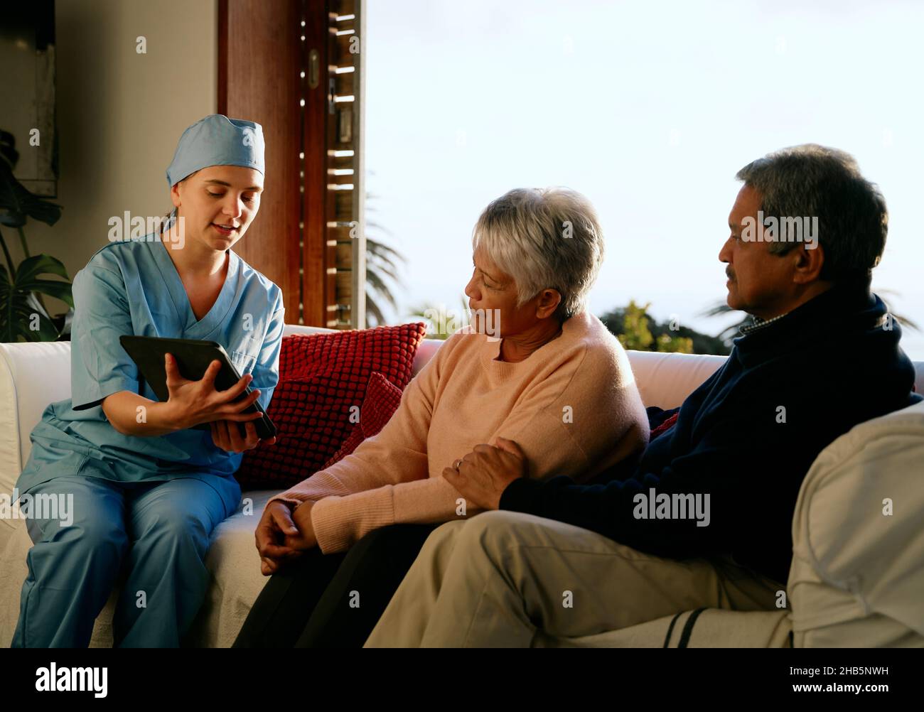 Medico che spiega la diagnosi a coppie anziane multietniche in consultazione a casa. Soggiorno moderno. Foto Stock