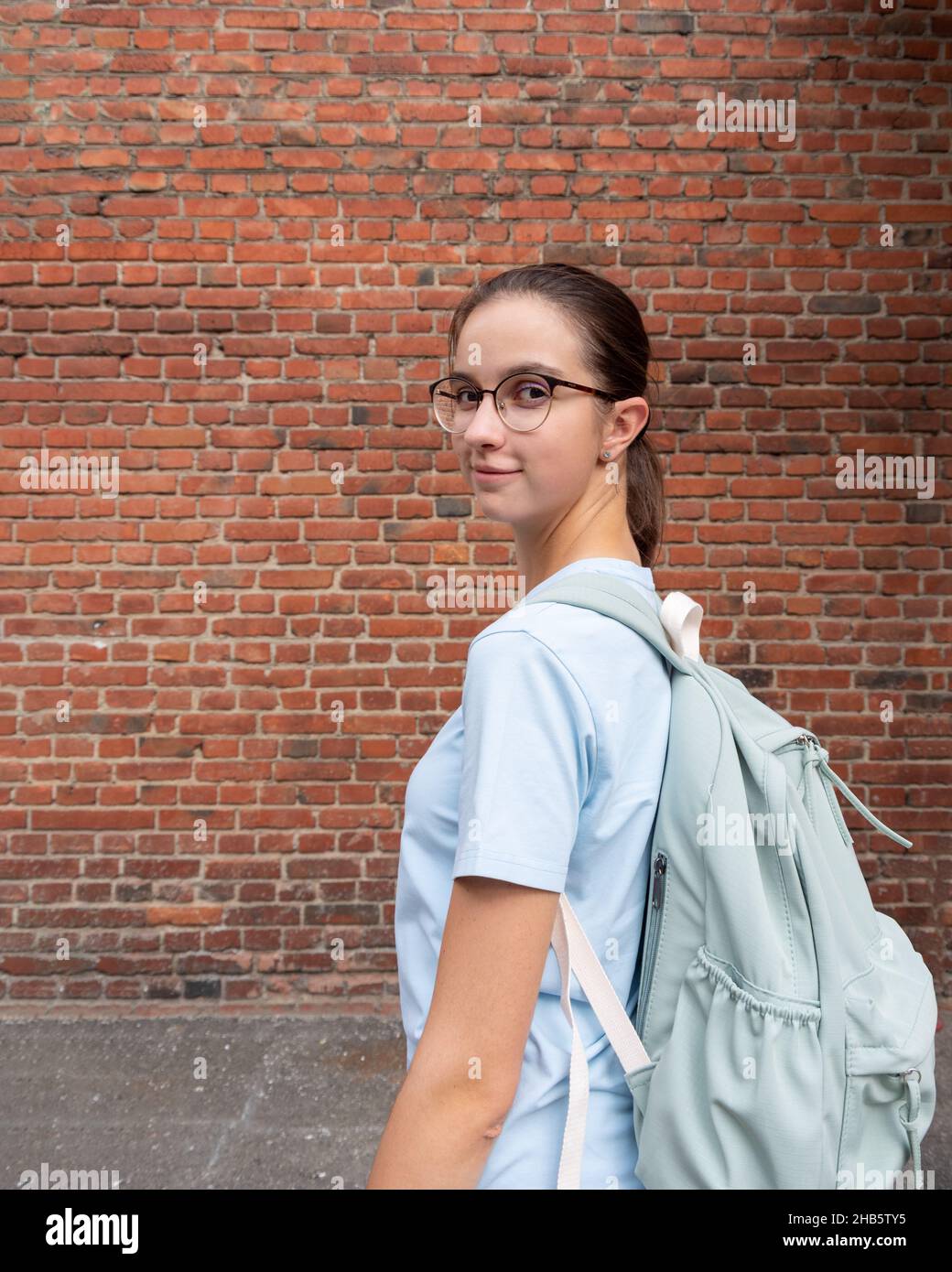 Ritratto di una studentessa ragazza in una T-shirt e con uno zaino blu su uno sfondo di un muro marrone mattone, spazio copia. Concetto di turismo studentesco. E Foto Stock