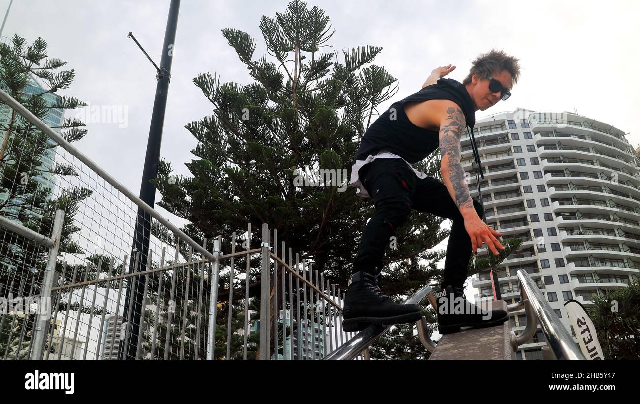 Bel ragazzo tatuato con occhiali da sole e capelli spiky surf sulle corrimano scala in Surfers Paradise, Gold Coast, Australia. Foto Stock