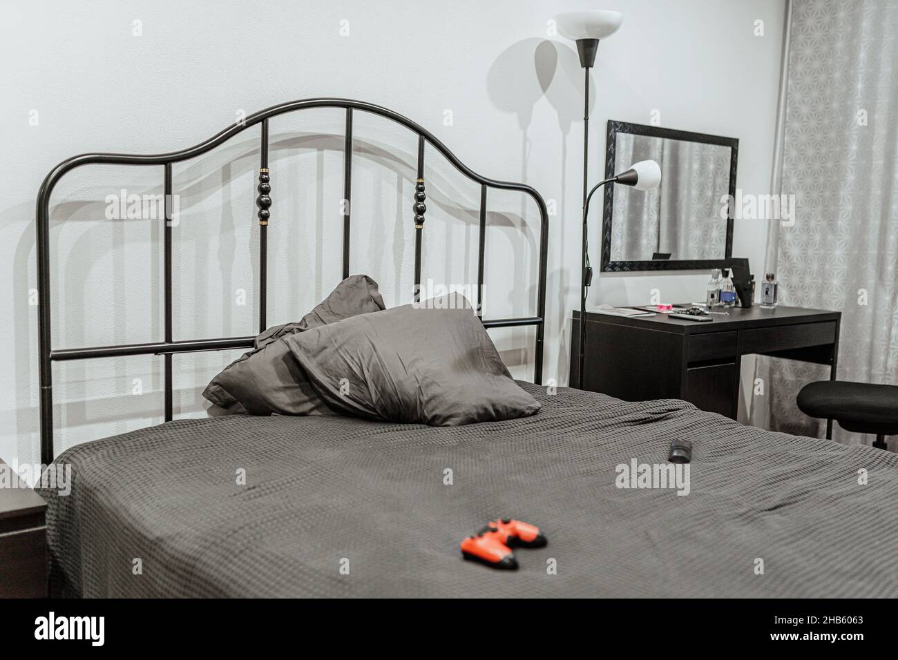 camera per ragazzi in tonalità di grigio non descritte con biancheria sgualcita sul letto e joystick per giochi, lampada da pavimento e scrivania. Sala giochi, interno sala teen Foto Stock