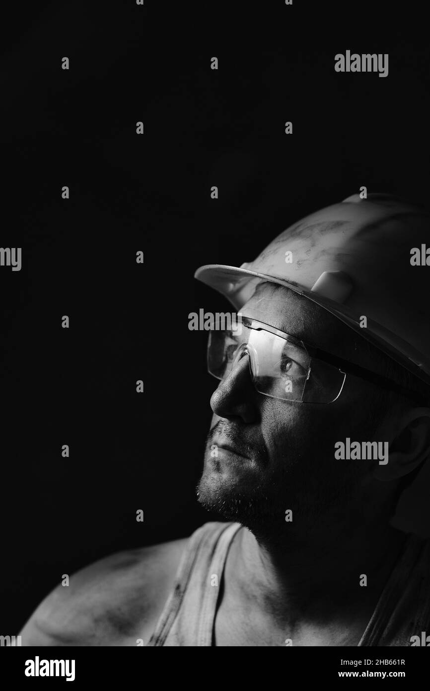 Ritratto del profilo di un minatore in un casco e occhiali, guardando la luce.Un lavoratore sporco in una camicia. Foto Stock