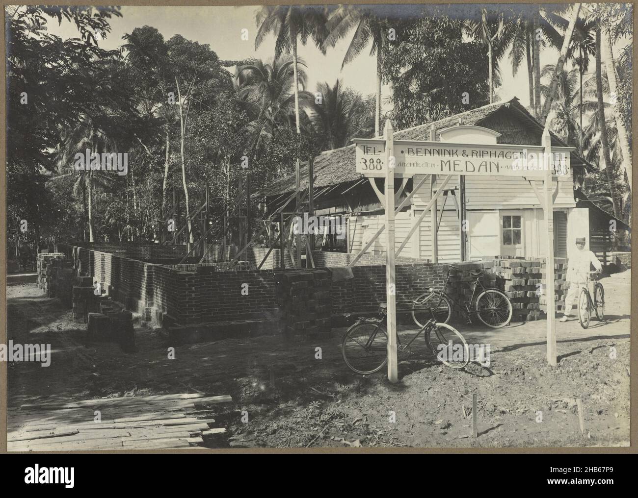 Progetto di costruzione, Un progetto di costruzione, probabilmente a Medan. Vicino ai primi muri di mattoni un segno della società di costruzione e alcune biciclette. Foto nell'album fotografico della ditta olandese Bennink e Riphagen a Medan negli anni ca. 1914-1919., anonimo, Medan, 1914 - 1919, supporto fotografico, stampa in argento gelatina, altezza 143 mm x larghezza 201 mm Foto Stock