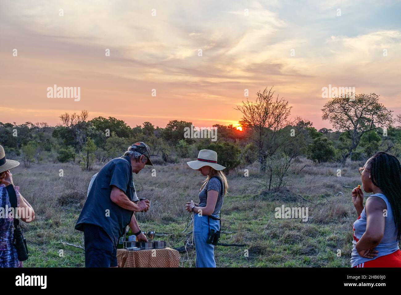 I turisti in un safari, safari, tra la fauna selvatica del Parco Nazionale Kruger, Sudafrica, bere un drink al tramonto Foto Stock
