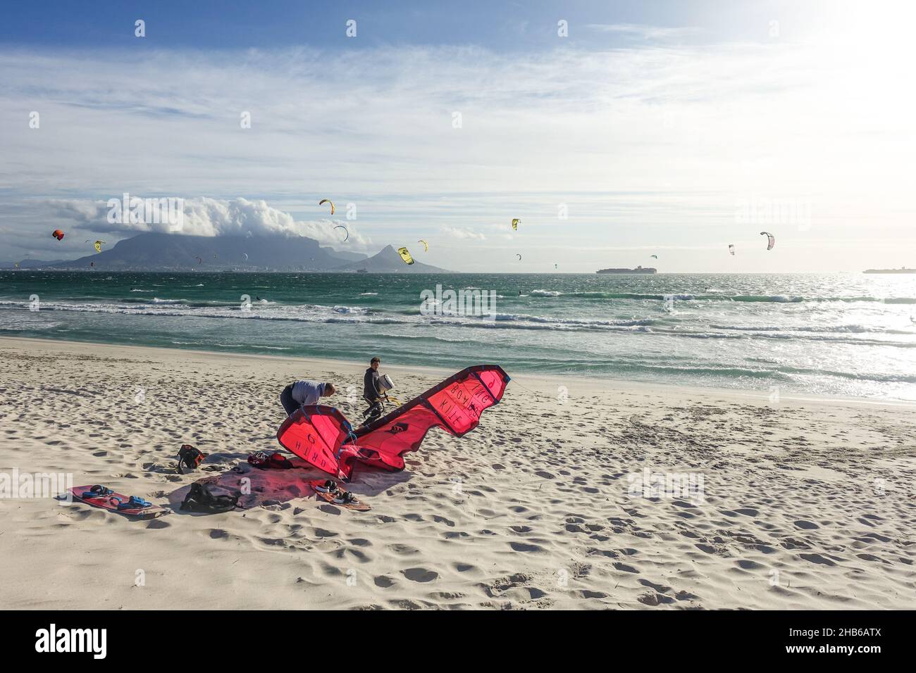 Kitesurfers che istituisce un aquilone rosso sulla spiaggia di Kite, Blouberg, Città del Capo, Sudafrica Foto Stock