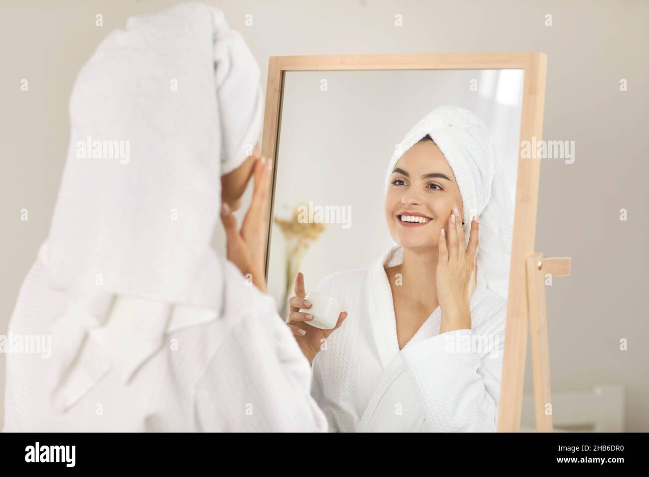 Ritratto di bella donna sorridente che dopo la doccia applica moisturizer sul viso. Foto Stock