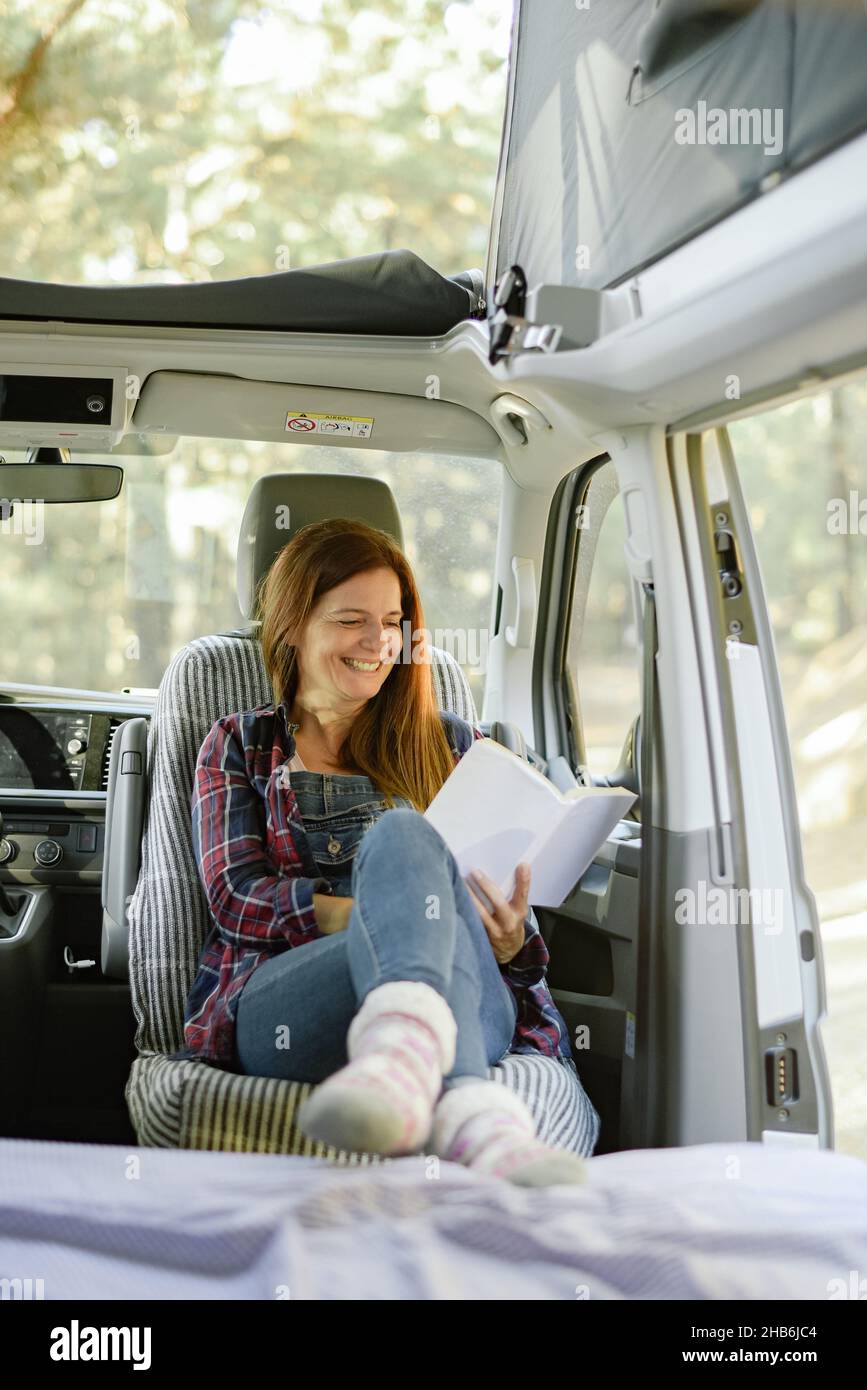 Viaggiando donna leggere libro in furgone parcheggiato Foto Stock