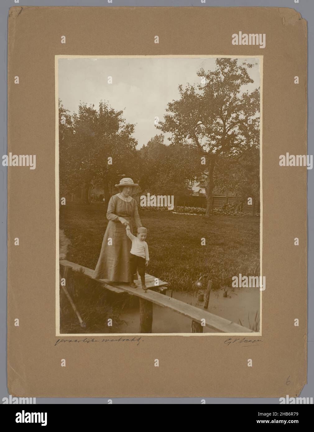 Ritratto di donna con ragazzo, camminando attraverso un asse sopra una fossa, Ritratto di donna con ragazzo, camminando attraverso un asse sopra una fossa. Sullo sfondo un giardino con alcuni alberi. La donna indossa un abito e un cappello estivo e guarda nella macchina fotografica, il ragazzo cammina avanti per la mano., G.V. Scagen (citato in oggetto), c.. 1900 - c. 1925, supporto fotografico, cartoncino, stampa in gelatina d'argento, altezza 230 mm, larghezza 169 mmaltezza 327 mm, larghezza 250 mm Foto Stock