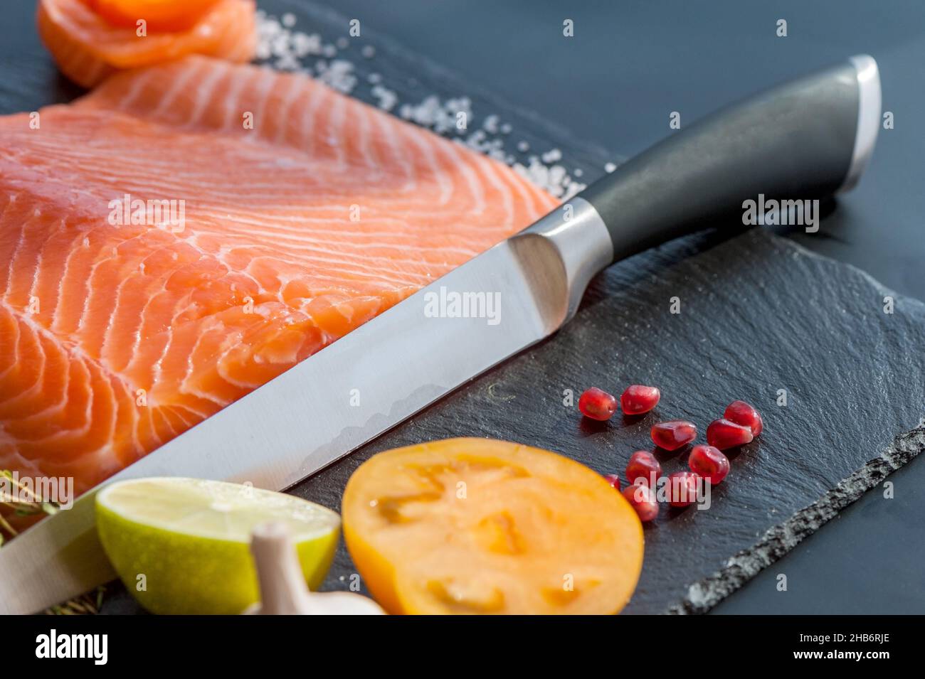 Lo chef usa il coltello per tagliare a fette il salmone crudo sul blocco di  tritare. Bistecca di filetto di salmone e condimenti sul tagliere nero Foto  stock - Alamy