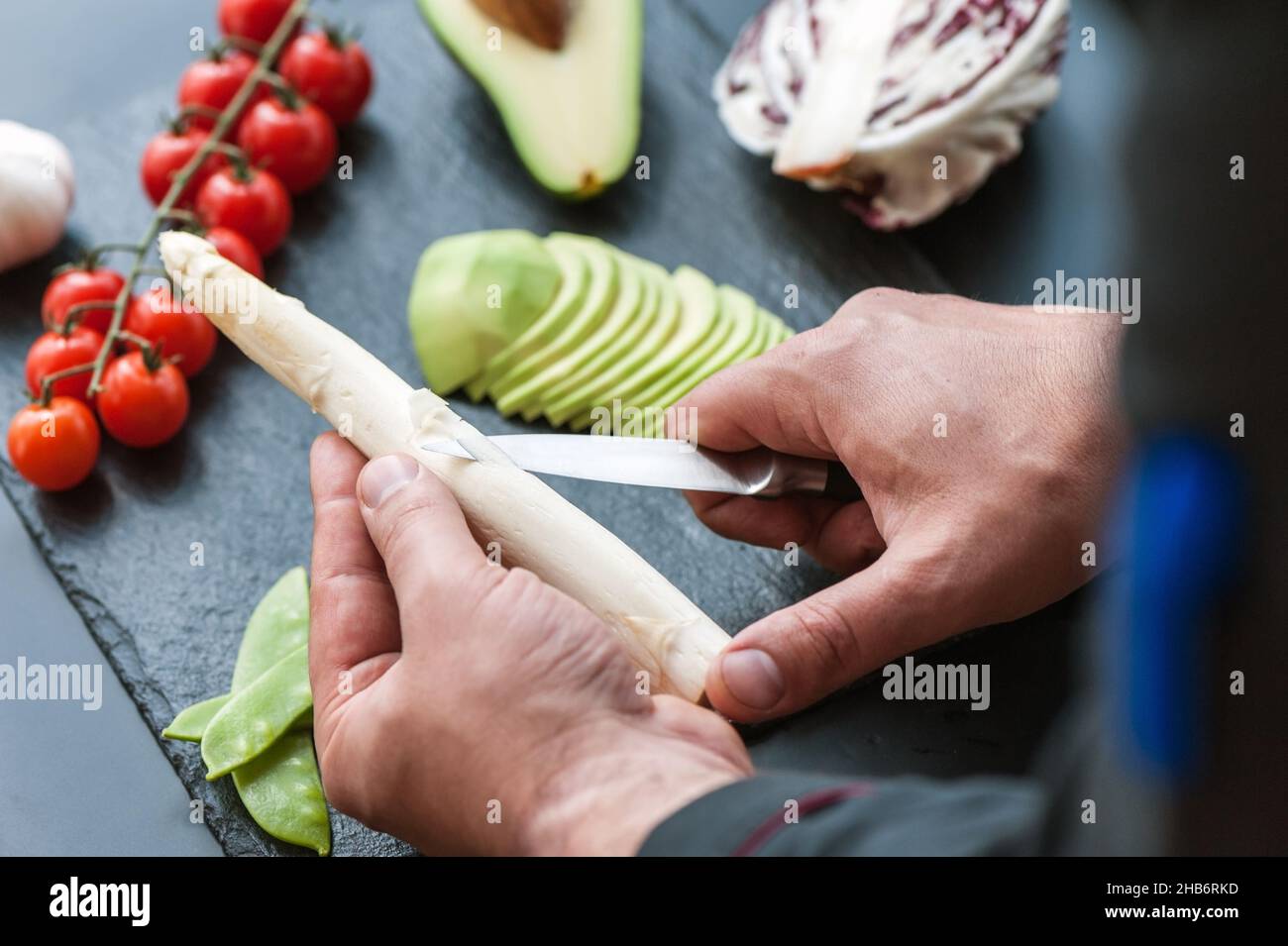 Spellatura manuale dei gambi di Asparagi con coltello, rimozione delle foglie esterne, pelo rifinito Asparagi giacenti su superficie scura Foto Stock