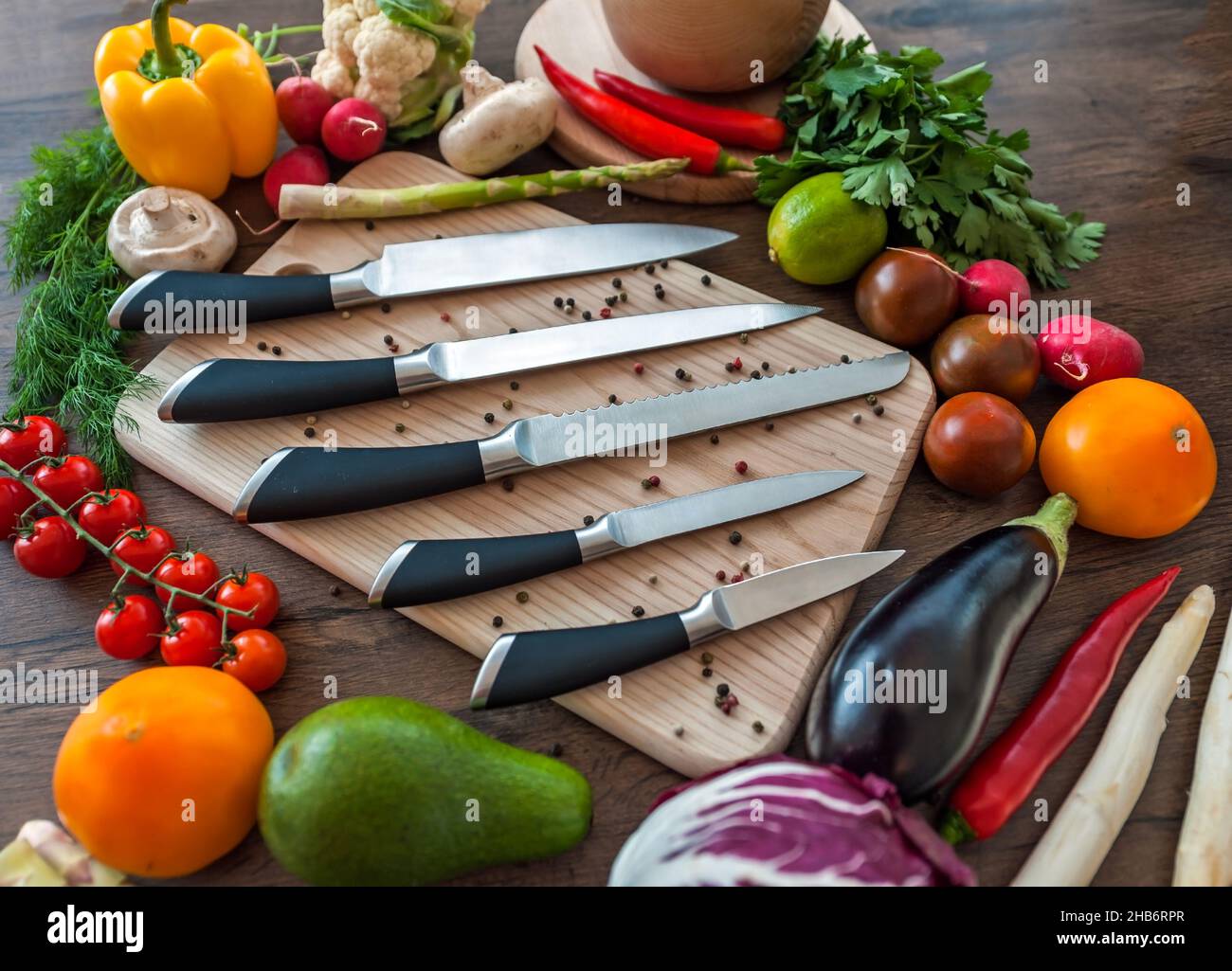 Chef Knifes su bordo di tritare in legno con verdure fresche sfondo. Concetto di cibo sano. Cibo vegetariano crudo Foto Stock