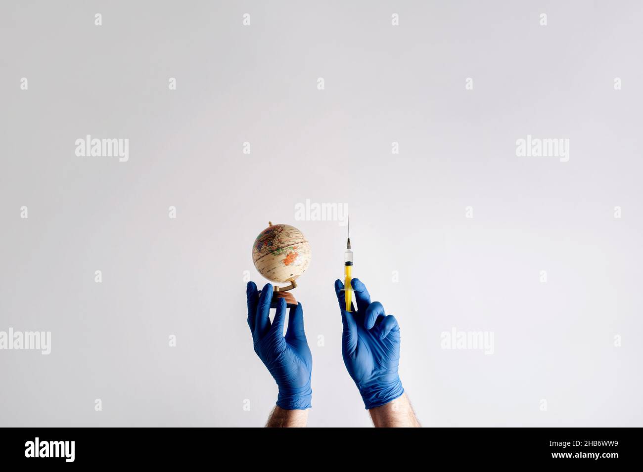 Simbolo dell'assicurazione malattia su scala globale. Mani in guanti medici con una siringa su sfondo bianco con spazio per la copia. Pandemia globale. Inf. Virale Foto Stock