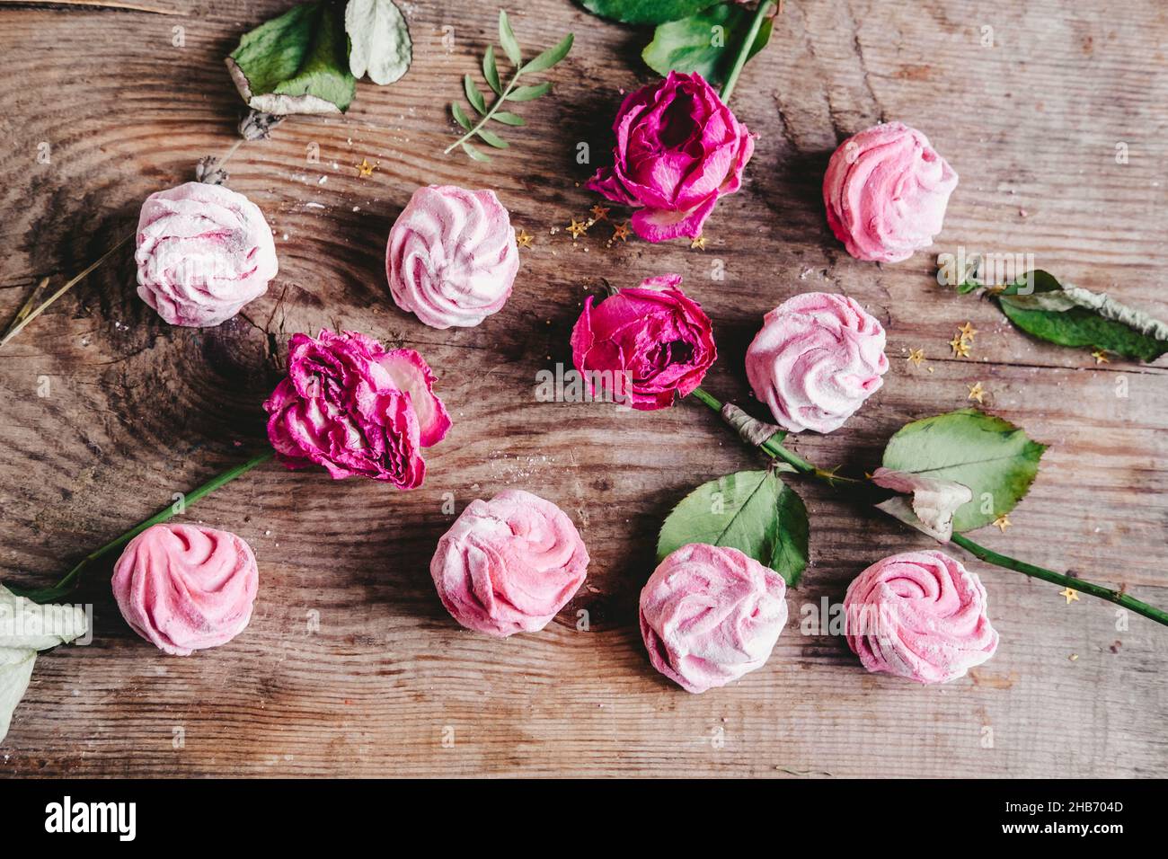 marshmallows rosa bacche assortite con boccioli di rose, su sfondo di legno. Fai-da-te elastico e morbido marshmallow Foto Stock