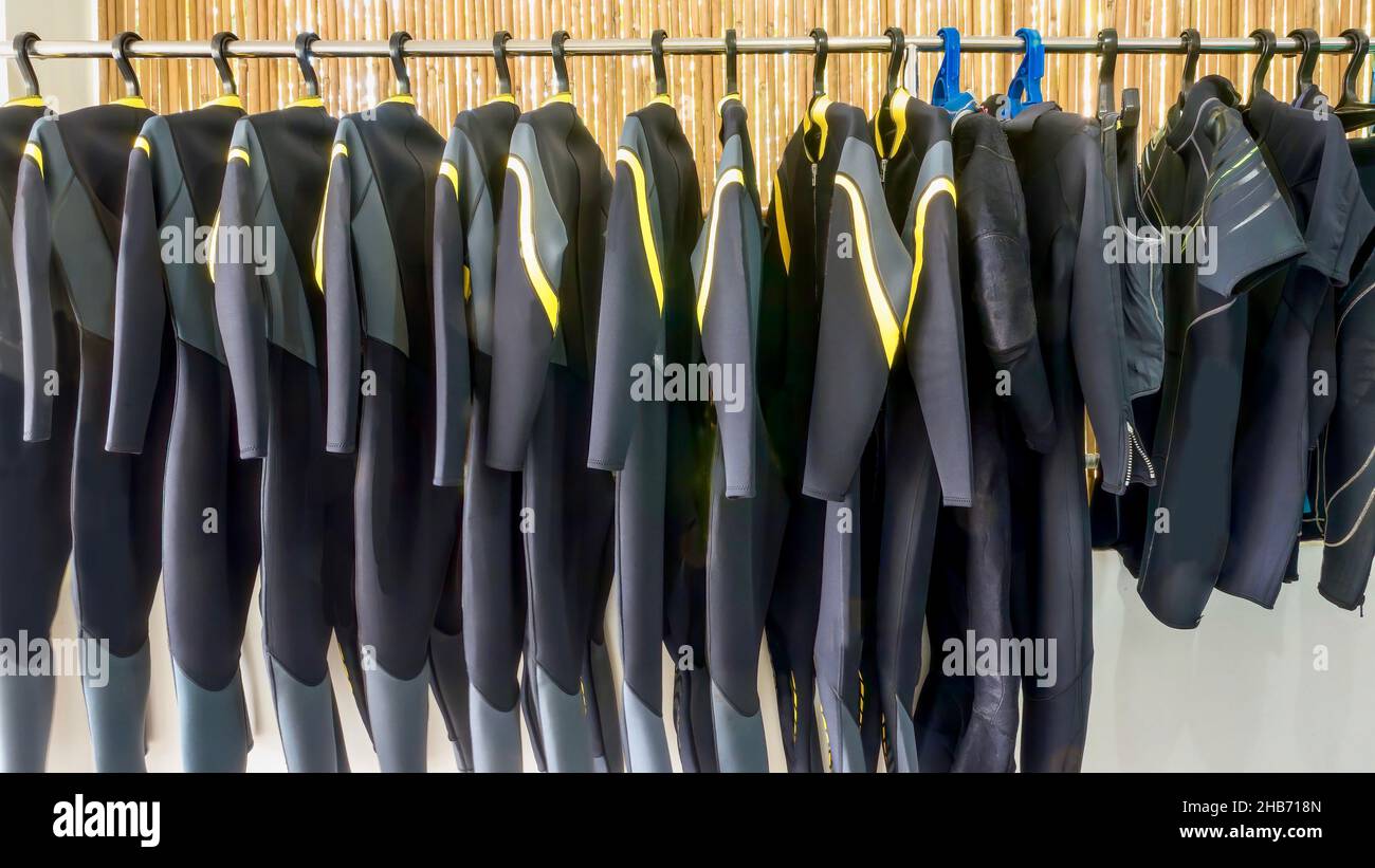 Una fila di mute da immersione in neoprene a lunghezza intera appese su una rastrelliera in un negozio di immersioni in un resort nelle Filippine. Foto Stock