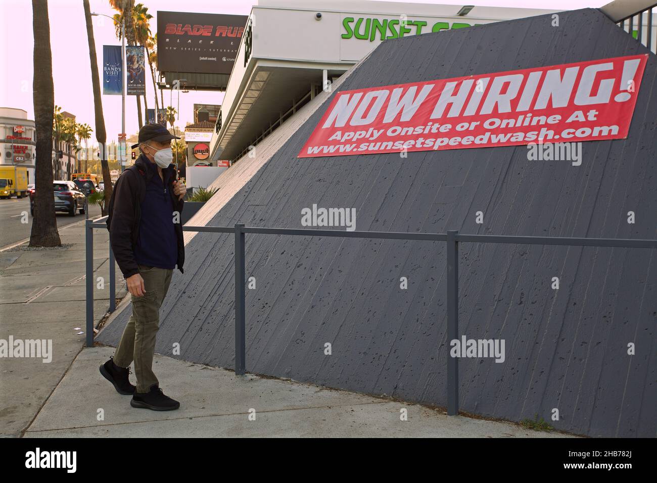 LOS ANGELES, STATI UNITI D'AMERICA - 10 dicembre 2021: Man Passing a Now Hiring banner on Sunset Boulevard in West Hollywood Foto Stock
