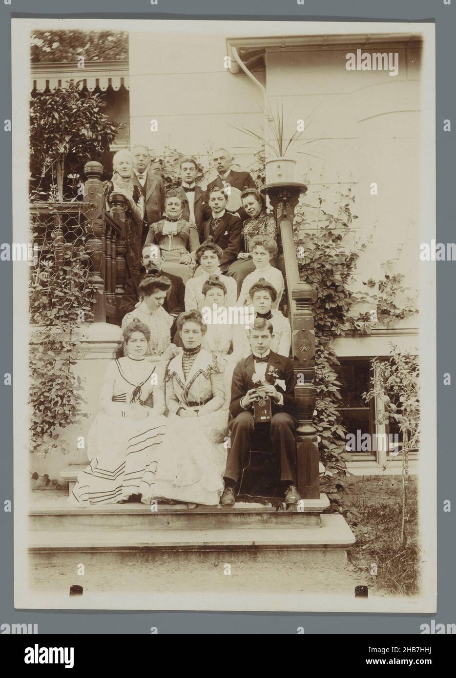 Ritratto di gruppo della famiglia Geertsema con Karel van den Berg seduto sulle scale dietro la casa, giovane uomo con macchina fotografica di fronte a destra, A.C.M. Geertsema, (cerchio di), Paesi Bassi, c.. 1895 - c. 1905, supporto fotografico, drager, :, altezza 176 mm x larghezza 126 mm Foto Stock