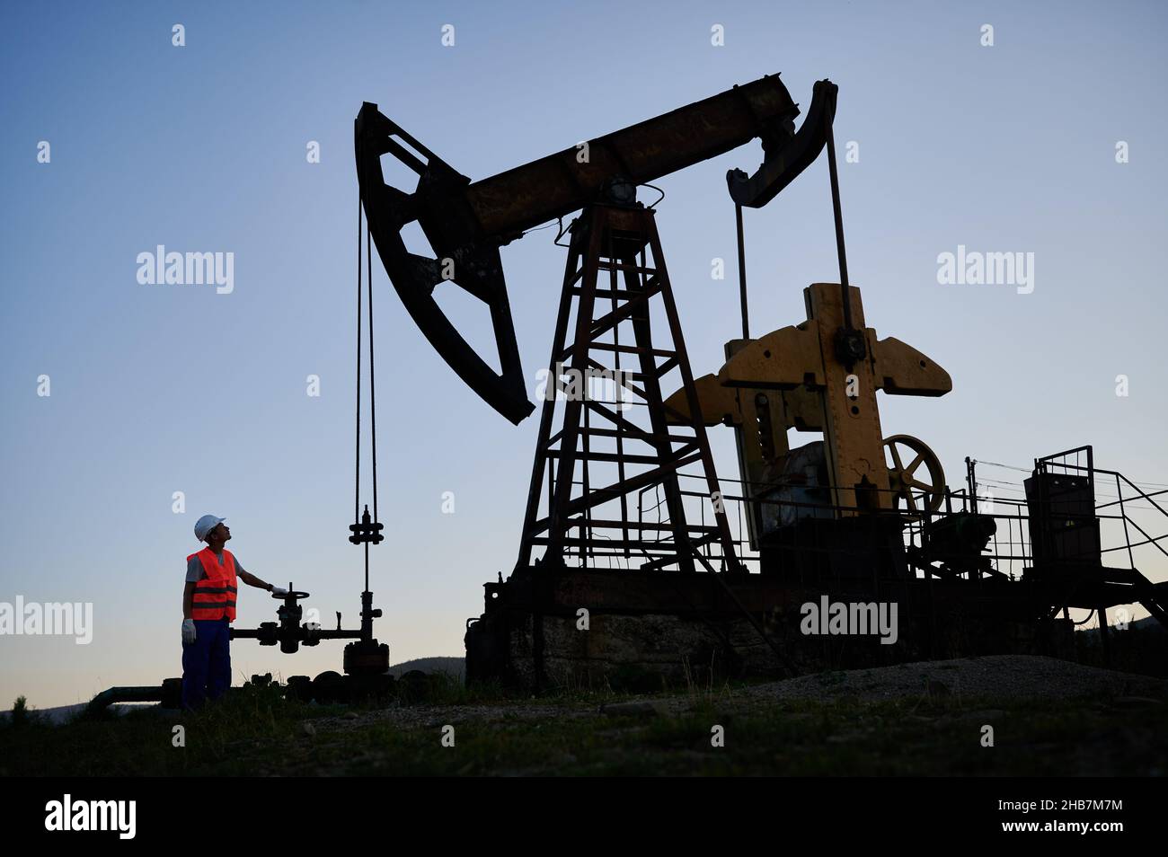 L'Oilman ha rilasciato una pressione eccessiva di gas nella conduttura dell'olio e ha osservato il funzionamento della pompa dell'olio. Operatore che garantisce l'estrazione sicura dell'olio. Trivellazione petrolifera in campo petrolifero per la produzione di petrolio da terra Foto Stock