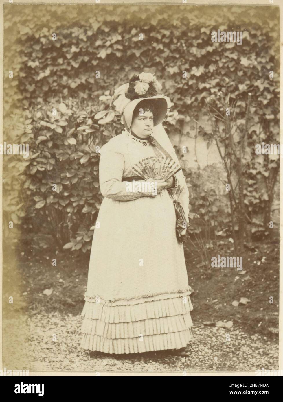 Ritratto di una donna francese con cappello e ventilatore, in piedi in un giardino, parte di album fotografico di un fotografo dilettante francese con foto di una famiglia, distilleria Delizy &amp; Doistau Fils, l'esercito e luoghi di interesse in Francia., anonimo, Francia, c. 1900 - c. 1910, carta, stampa albume, altezza 152 mm x larghezza 115 mm Foto Stock