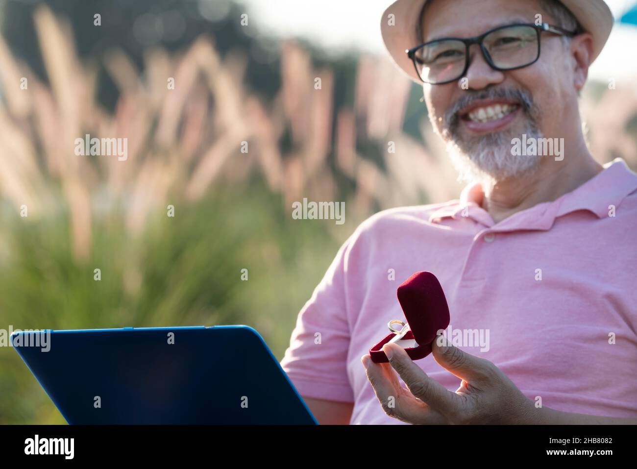 Happiness Man sorpresa matrimonio proposta online per ragazza online attraverso il computer portatile. Pensione barba grigia matura o uomo anziano in rosa e cappello Foto Stock